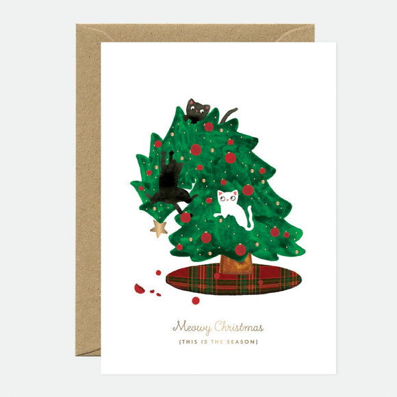 A Christmas greeting card with a illustration of a Christmas tree decorated with red berries and white balls, accompanied by black and white cats. The card has 'Merry Christmas' text and is accompanied by a brown envelope.