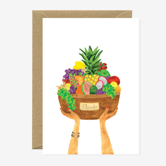 A greeting card featuring a illustration of hands holding a basket filled with various fruits and vegetables, with gold foil details, and a blank interior.
