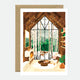 A greeting card depicting a cozy indoor scene with a fireplace, bookshelves, and a view of a snowy landscape through large windows.