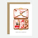 Greeting card with an illustration of a cat inside an open suitcase, surrounded by travel-related items like a map and sunglasses, with the text 'TRAVEL WITH ESSENTIALS' at the bottom.