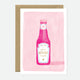 A greeting card with an illustration of a ketchup bottle on a pink background, with the text 'let's KETCHUP soon' on it. There is a brown envelope behind the card.