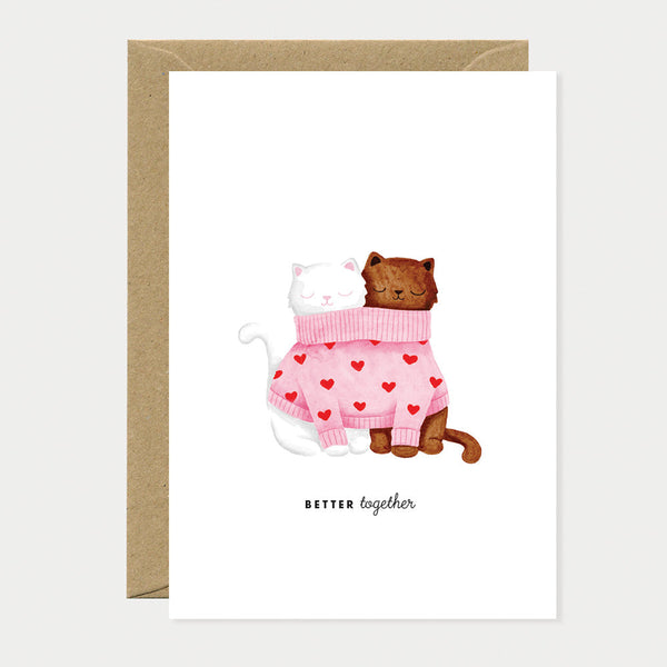 Greeting card showing two cats cuddling together in one pink sweater with red hearts, symbolizing love, unity, and warmth.