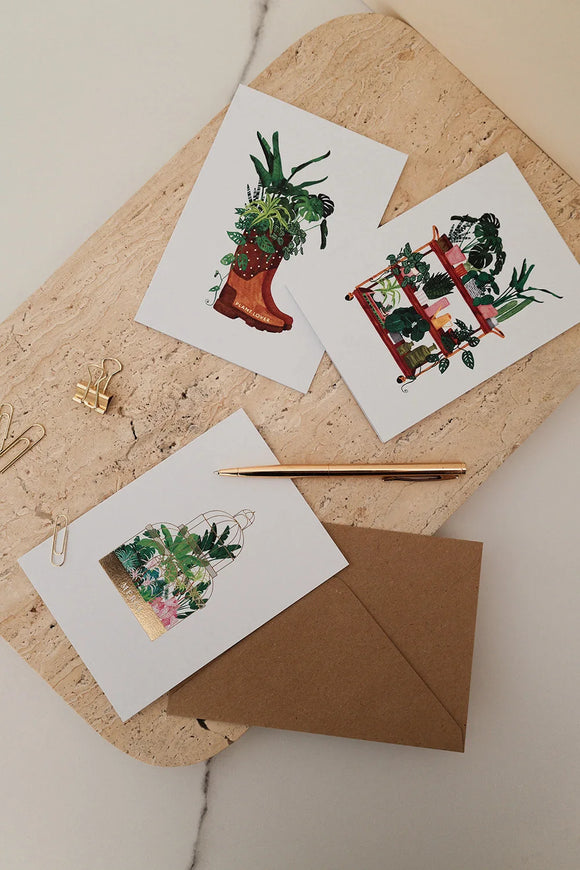 Botanical greeting cards with plant illustrations, styled on stone board with kraft envelope, gold pen, and paper clips.