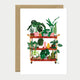 Greeting card showing a plant shelf cart filled with different houseplants, pots, and watering cans in a colorful botanical arrangement.