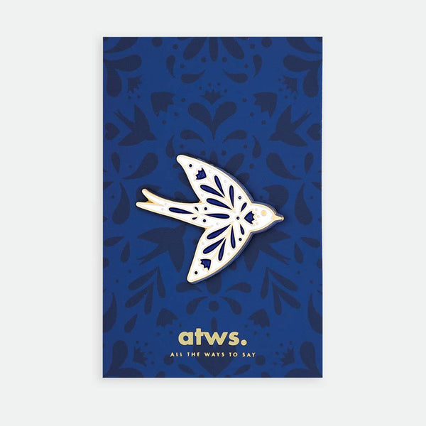 Swallow enamel pin by All the Ways to Say featuring gold-plated blue and white swallow design on dark blue illustrated floral background.