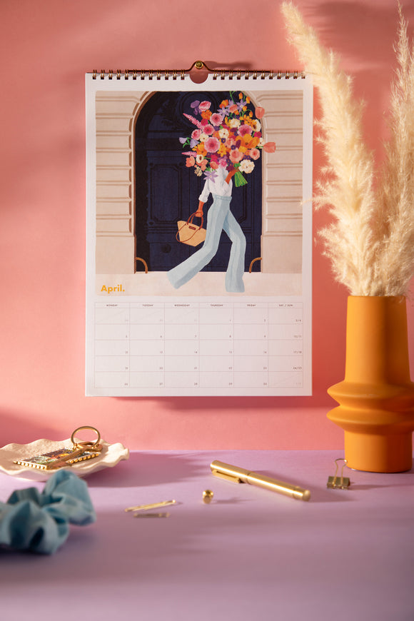 April page of the 2027 ATWS wall calendar: woman carrying a giant flower bouquet in front of a navy Paris door