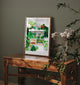 Lombok art print leaning on a rustic wooden table with green plants in a natural interior setting