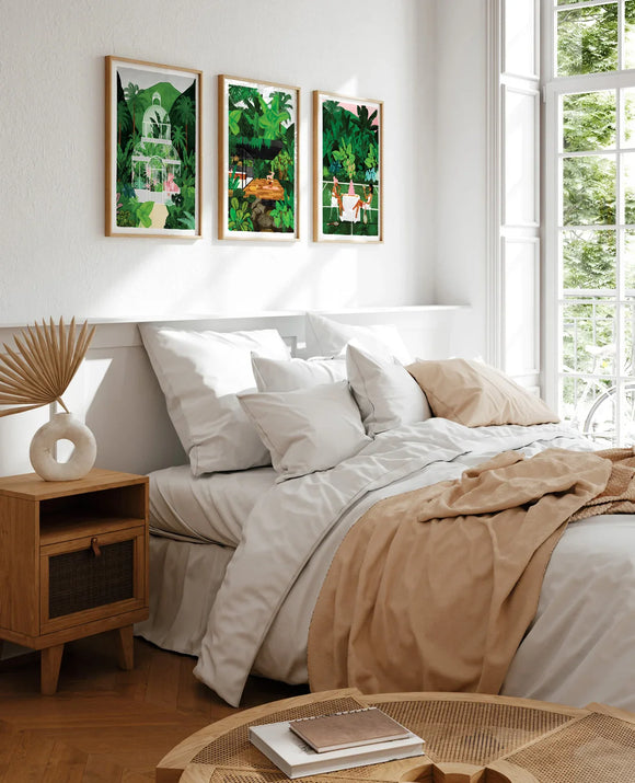 Set of three Namaster tropical art prints framed above a bed with neutral bedding and soft light