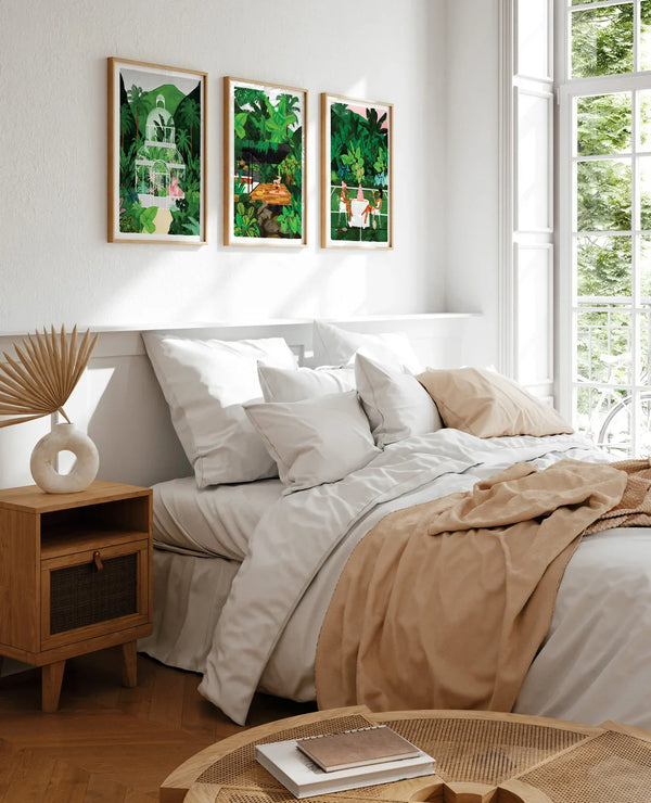 Set of three Namaster tropical art prints framed above a bed with neutral bedding and soft light
