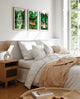 Set of three Namaster tropical art prints framed above a bed with neutral bedding and soft light
