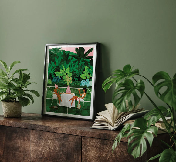 Tennis Court art print framed on a dark wooden cabinet surrounded by tropical green plants