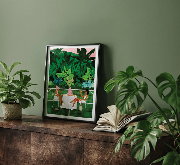 Tennis Court art print framed on a dark wooden cabinet surrounded by tropical green plants