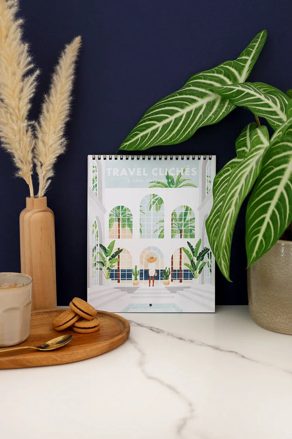 Travel Clichés 2026 calendar by All The Ways To Say displayed with green plants and navy background