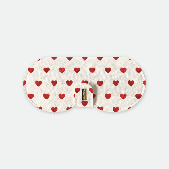 White glasses case with red hearts pattern and gold logo plate on clasp displayed on a light background