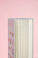Side view of Dogue notebook spine with pink title and lined interior pages against soft pink background.