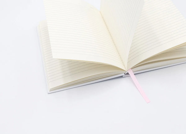 Dogue notebook open with lined cream pages and pink ribbon, showing flipping sheets on white background.