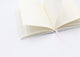 Dogue notebook open with lined cream pages and pink ribbon, showing flipping sheets on white background.