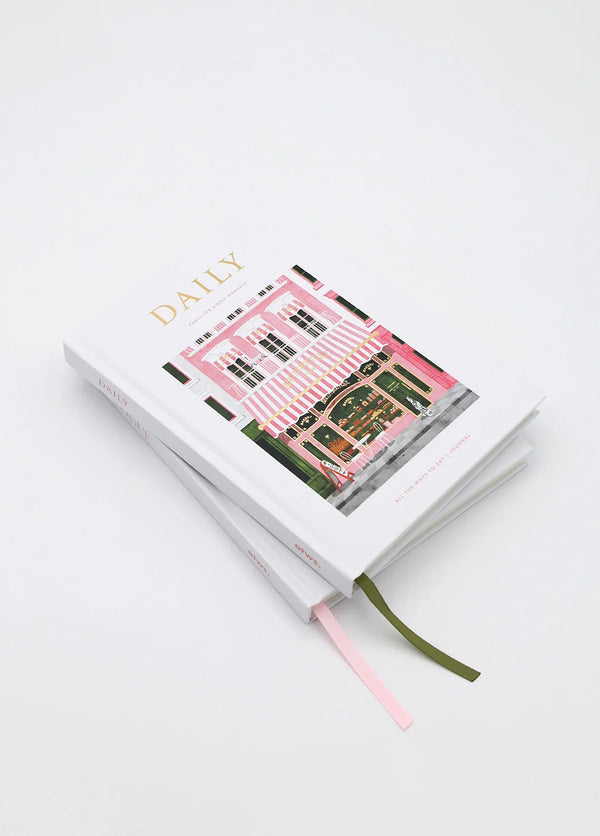 Stack of Daily bakery notebooks with illustrated pink storefront cover and ribbon bookmarks in pink and green.