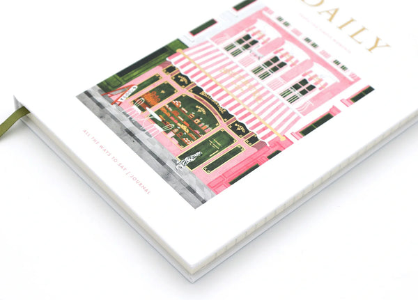 Daily hardcover notebook with bakery illustration laying flat, showing gold foil title and green ribbon bookmark.