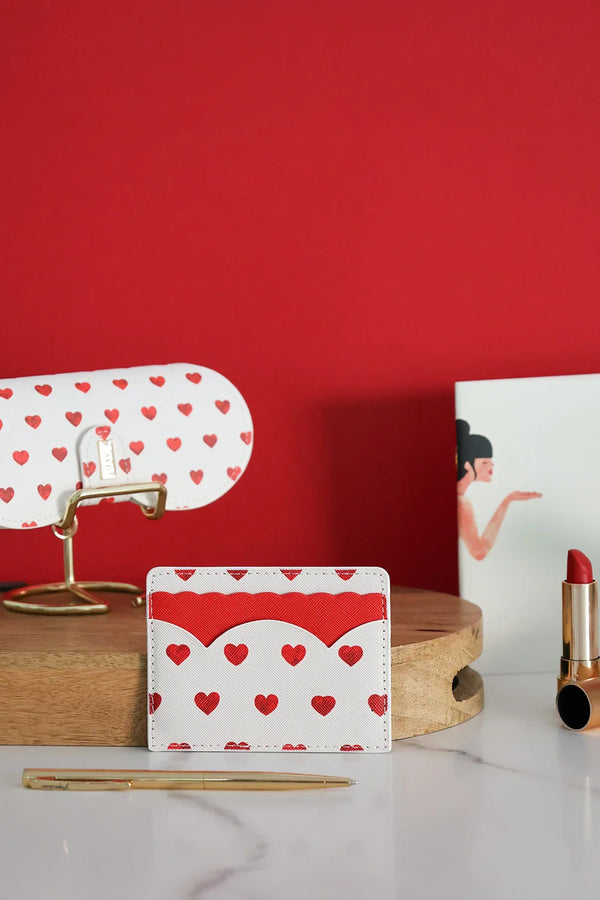 Romantic red hearts card holder styled with matching eyeglass case, lipstick, and gold pen on marble surface.