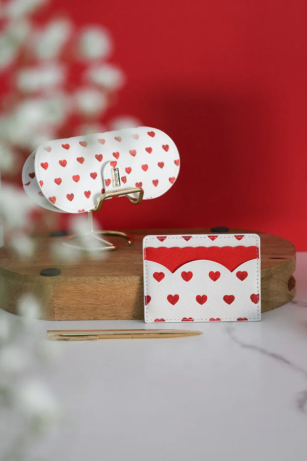 Red hearts card holder and matching eyeglass case displayed on wooden stand with gold pen against red background.