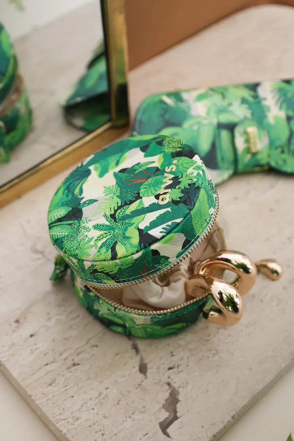 Round jewelry box with tropical green leaves pattern, displayed next to matching sunglasses case