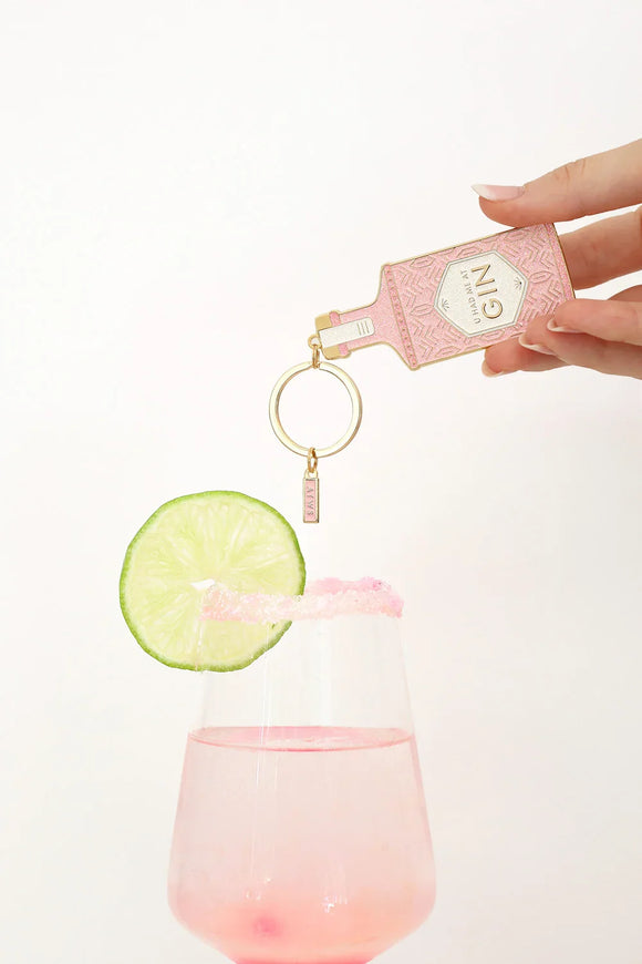 Pink gin bottle keychain with gold accents held above a cocktail glass with lime