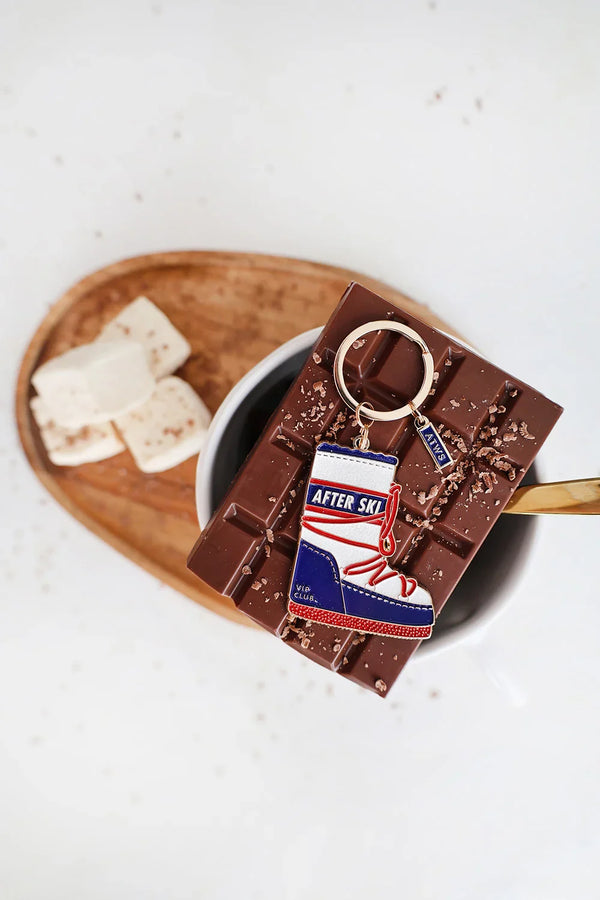 After Ski keychain by All The Ways To Say placed on a chocolate bar over a cup of hot cocoa
