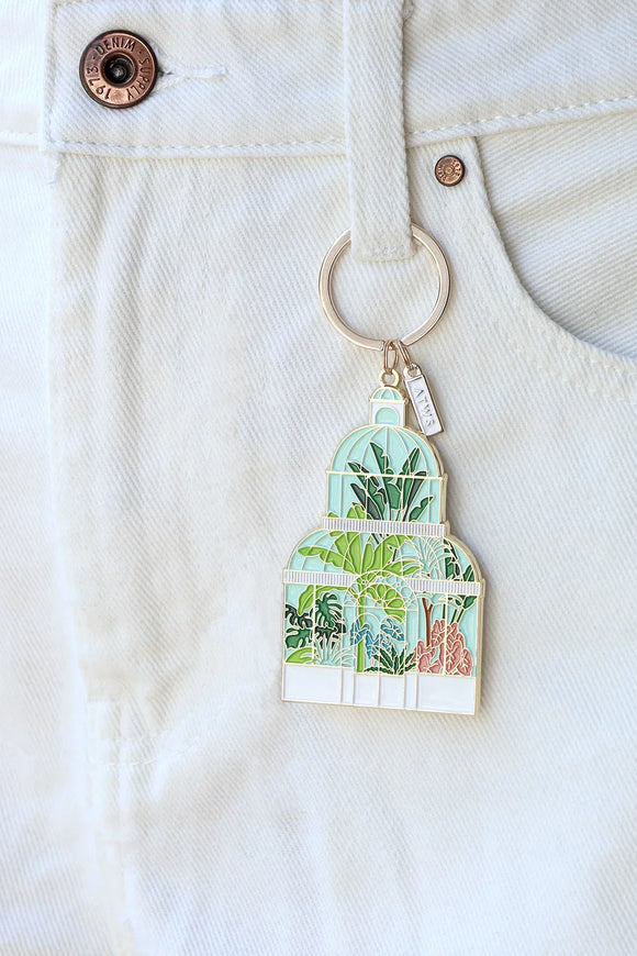 Green House keychain by All The Ways To Say hanging on white denim pocket – botanical enamel design