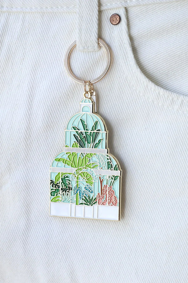 Close-up of Green House enamel keychain by All The Ways To Say – glasshouse with tropical plants illustration