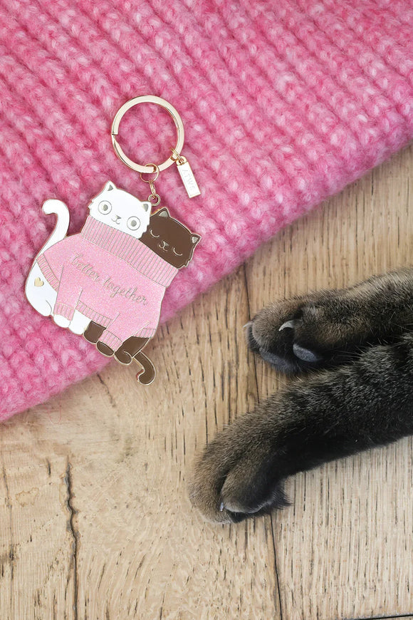 Enamel keychain 2 Cats in a Sweater by All The Ways To Say next to cat paws on wooden floor