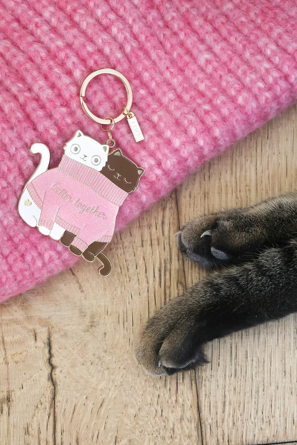 Enamel keychain 2 Cats in a Sweater by All The Ways To Say next to cat paws on wooden floor