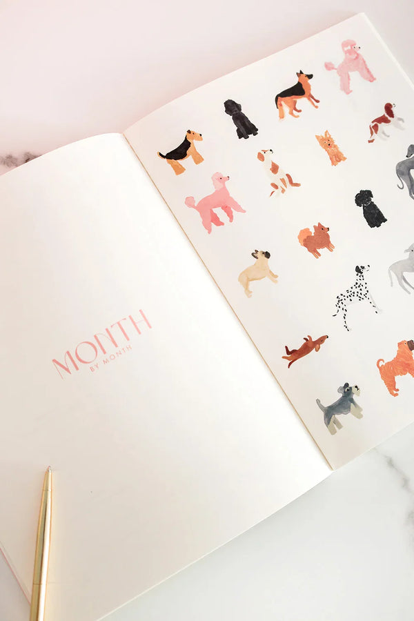 Inside view of the Dogue monthly planner featuring watercolor dog illustrations and pink “Month by Month” title on a clean white page.