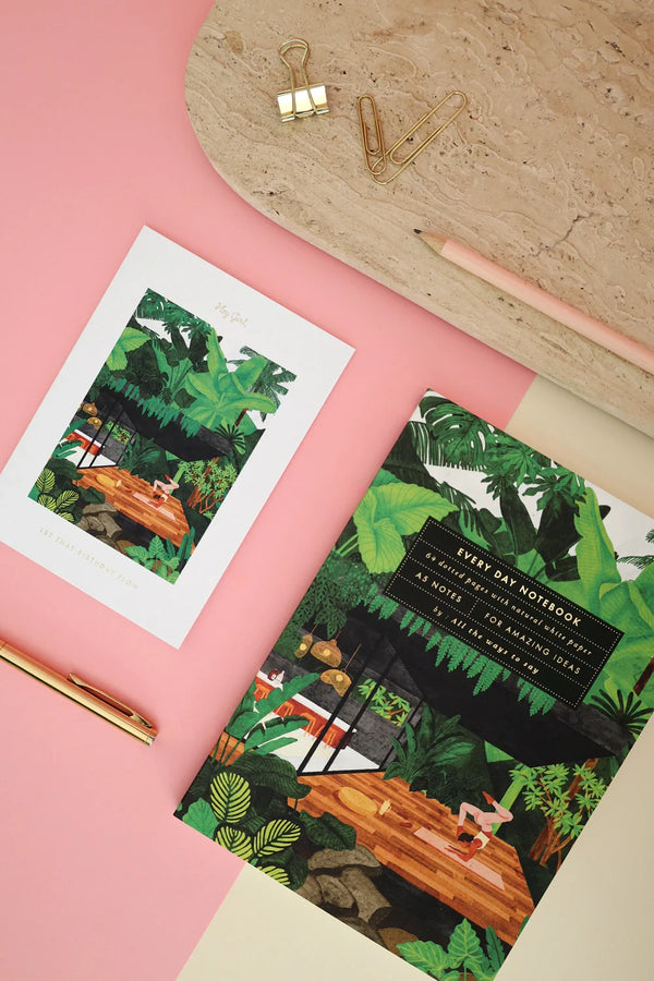 Yoga retreat illustrated notebook styled with gold pen, clips, and postcard on pink background for creative stationery flatlay.