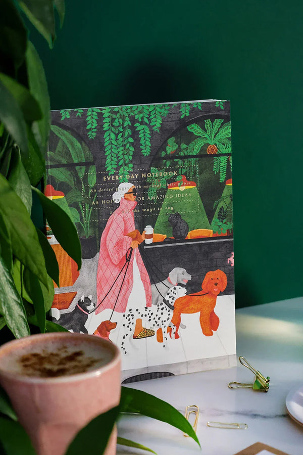 Dog Lover notebook featuring a woman walking dogs illustrated with green plants and cozy café scene – All the Ways to Say.