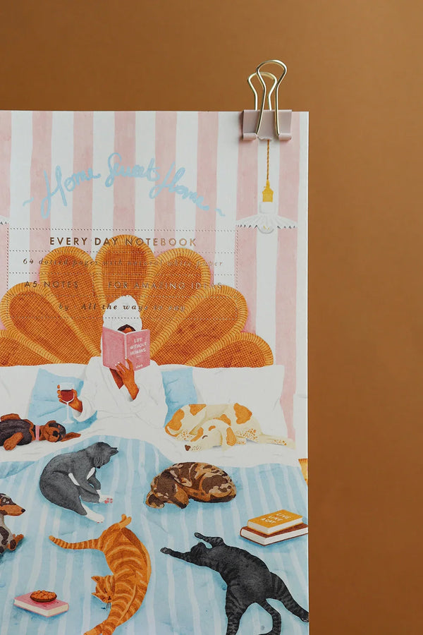 All The Ways To Say Home Sweet Home notebook close-up – woman with coffee and pets relaxing on striped blue bedspread