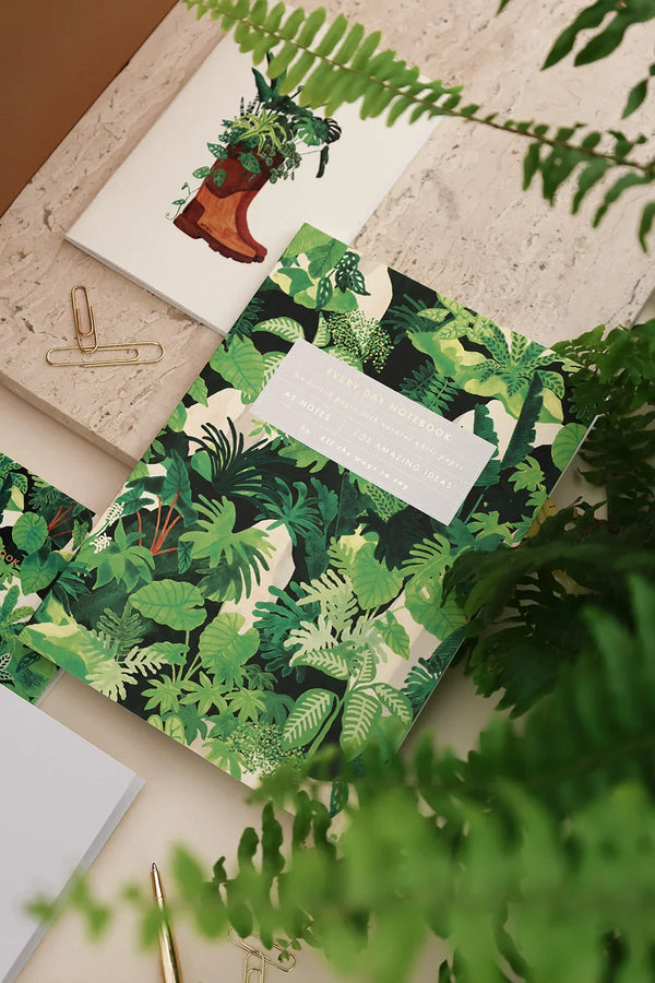 Close-up of Green Cliff notebook by All the Ways to Say featuring vibrant green jungle leaves design with gold details on a beige stone background.