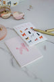 Dogue notebook with illustrated dog breeds on white cover, styled with gold pen and pink sunglasses for a chic desk setup.