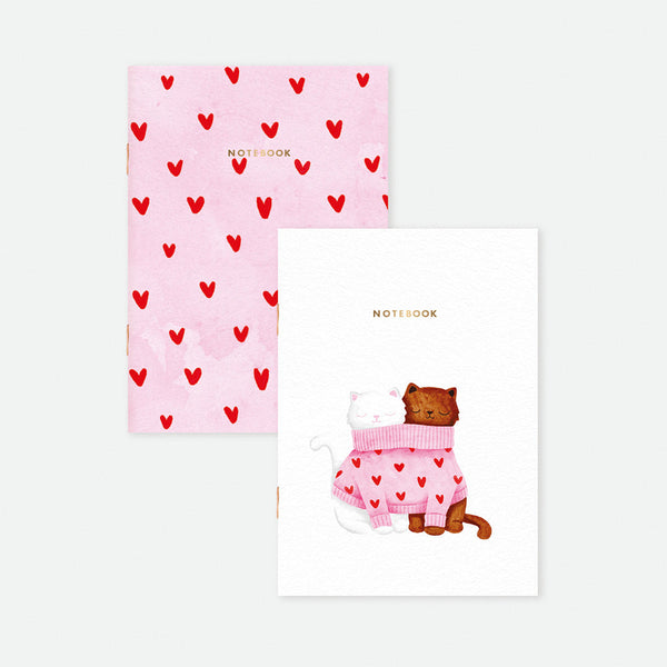 Set of two A6 pocket notebooks, one with two cats sharing a pink heart sweater, the other with pink cover and scattered red hearts, gold foil detail.