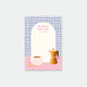 A notepad with a coffee-inspired design, featuring an illustration of a coffee cup and pot on a pink surface, with a blue grid pattern at the top where the text 'BLACK COFFEE' is written.