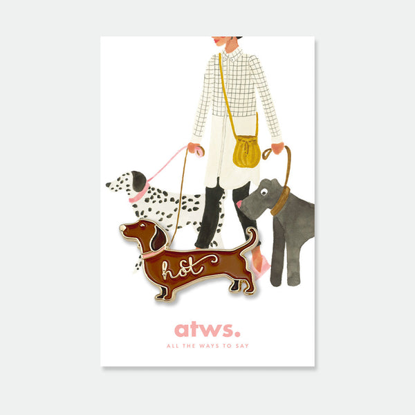 Hot Dog enamel pin by All the Ways to Say featuring brown dachshund with gold-plated finish and “hot” script on illustrated dog-walking background.