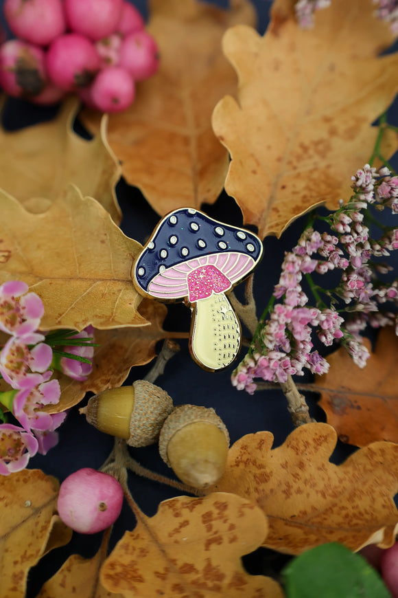 Close-up of Crazy Mushroom enamel pin by All The Ways To Say – navy cap, pink gills, and gold details on leaf background