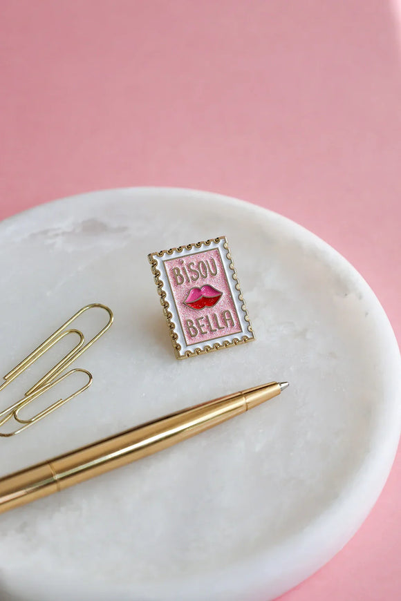 Bisou Bella enamel pin by All The Ways To Say on marble tray with gold pen and paper clips – pink background lifestyle photo