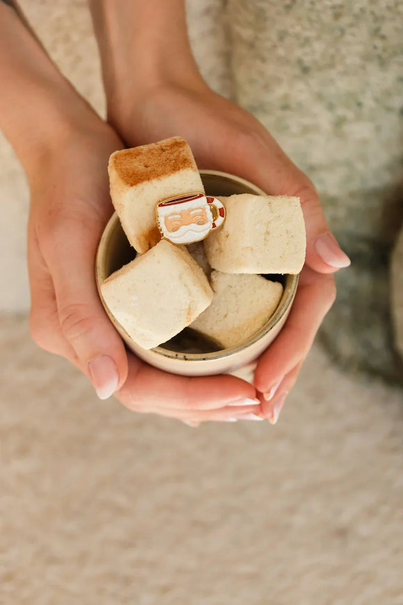 Close-up of Santa’s Cup enamel pin by All The Ways To Say – red and white mug design with Santa face on fluffy marshmallows