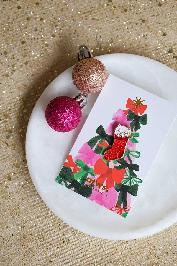 Cat Sock enamel pin by All The Ways To Say on festive card with Christmas ornaments – glitter background
