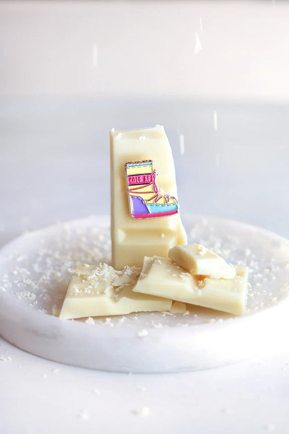 Cold AF enamel pin by All The Ways To Say on white chocolate pieces with coconut flakes – playful winter aesthetic