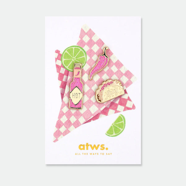 Spicy set of 3 enamel pins by All the Ways to Say featuring taco, chili pepper and hot sauce designs with gold-plated details on checkered pink card.