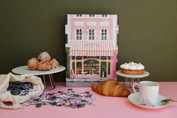 Pink Bakery puzzle by All the Ways to Say displayed with pastries and croissant on a pink table — charming Parisian bakery illustration with gold details.