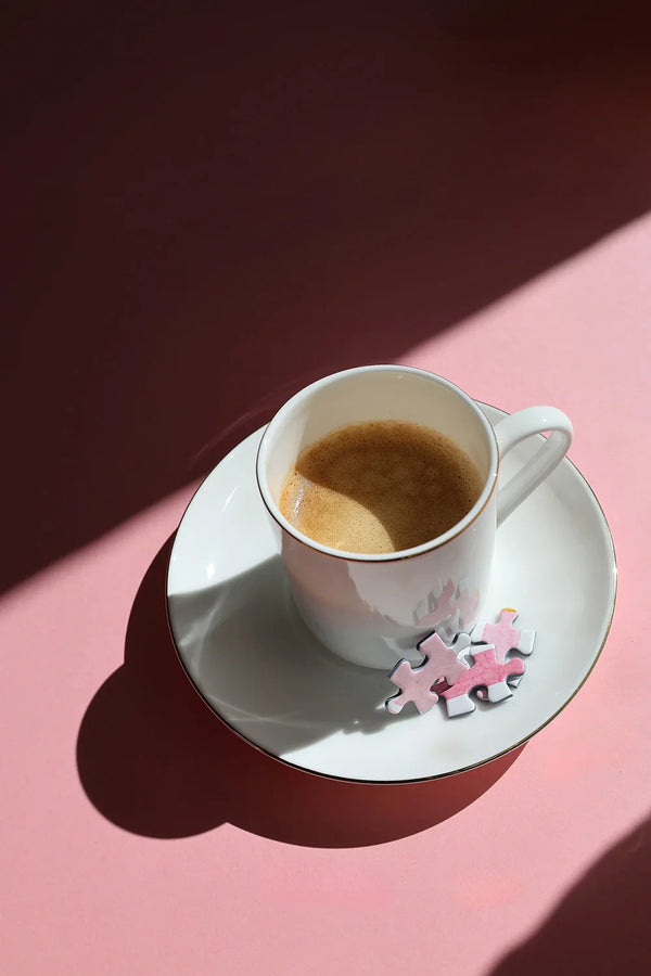 Full breakfast scene with croissant, pastries, coffee and Pink Bakery puzzle by All the Ways to Say on a pink and olive background.
