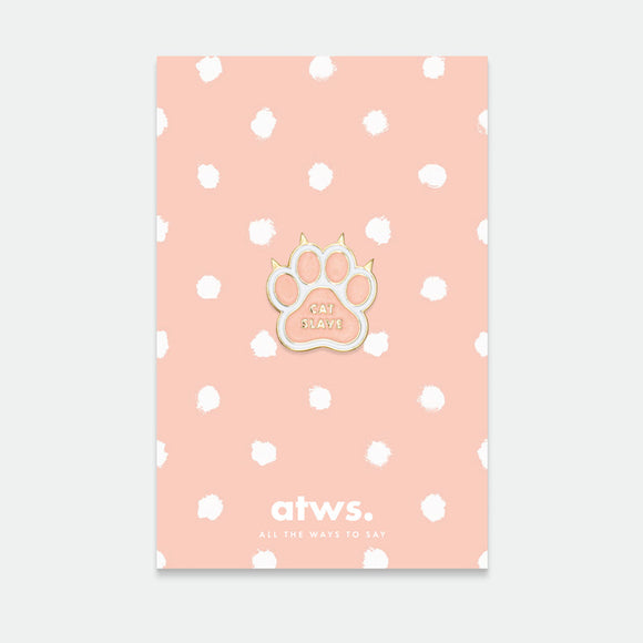A gold plated enamel pin in the shape of a cat paw, displayed on a card with a pink polka dot background.